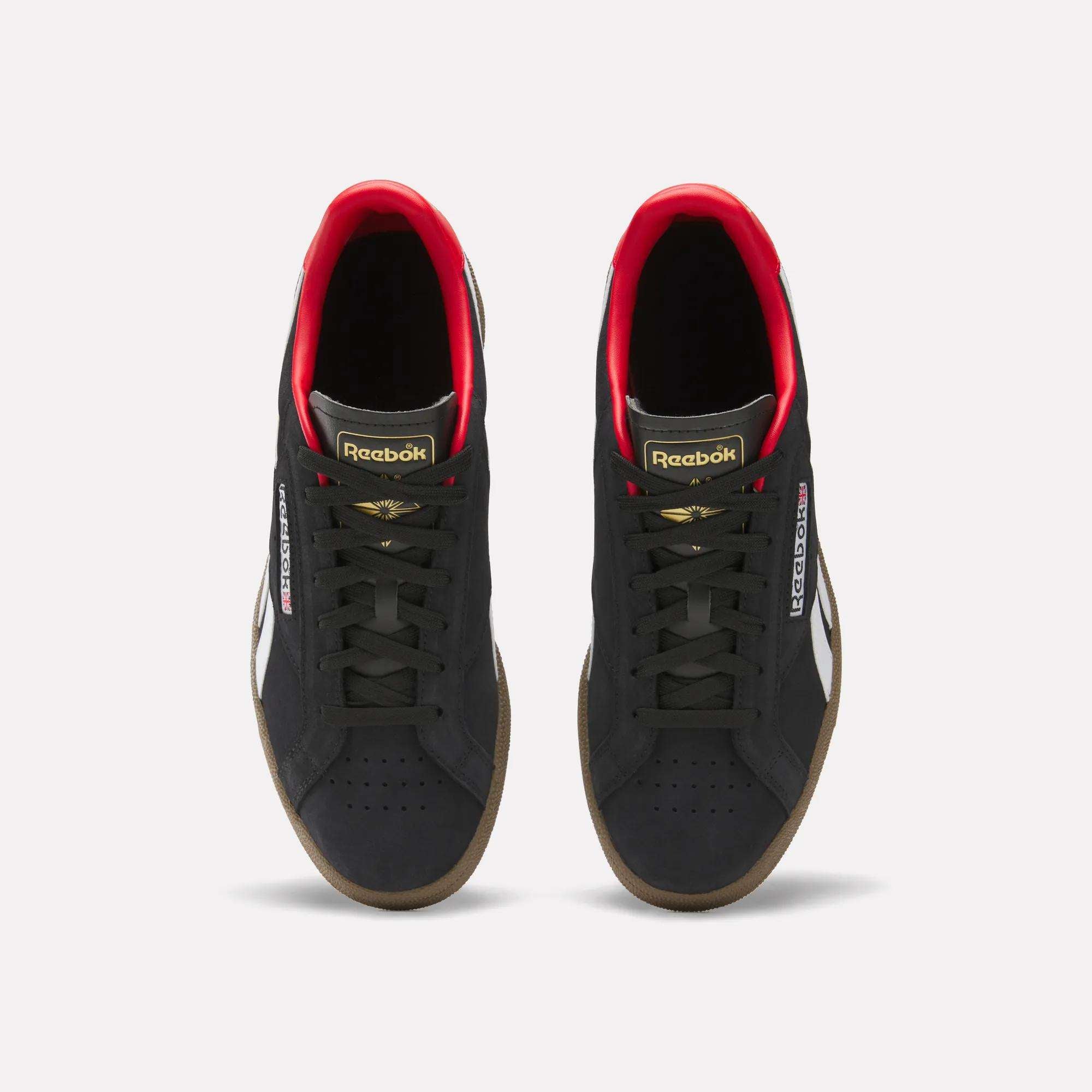 A pair of Reebok Club C Grounds UK Shoes in black with white side stripes, gold and red accents, black laces, and gum soles are shown from above on a white background—a perfect classic tennis-style casual shoe.