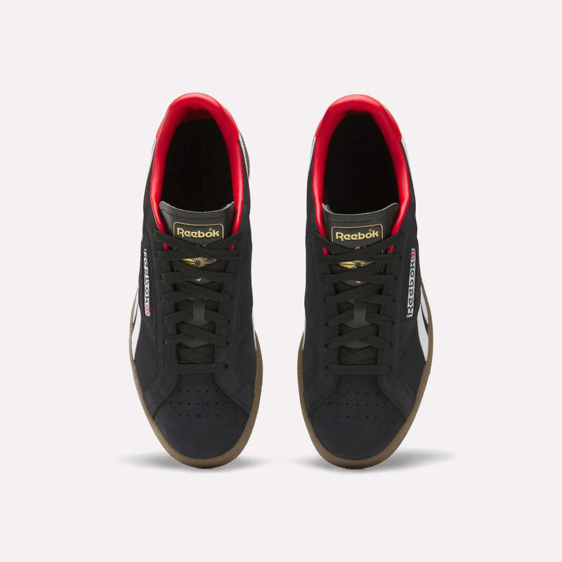 A pair of Reebok Club C Grounds UK Shoes in black with white side stripes, gold and red accents, black laces, and gum soles are shown from above on a white background—a perfect classic tennis-style casual shoe.