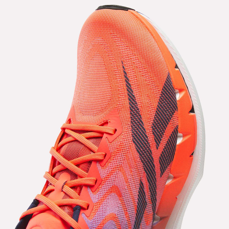 A close-up of the Reebok SpeedShifter Running Shoe highlights its vibrant orange color, black diagonal stripes, matching orange laces, and a white sole with visible grooves and textured detailing. The shoe features responsive HyperFloat foam in the sole for enhanced comfort.
