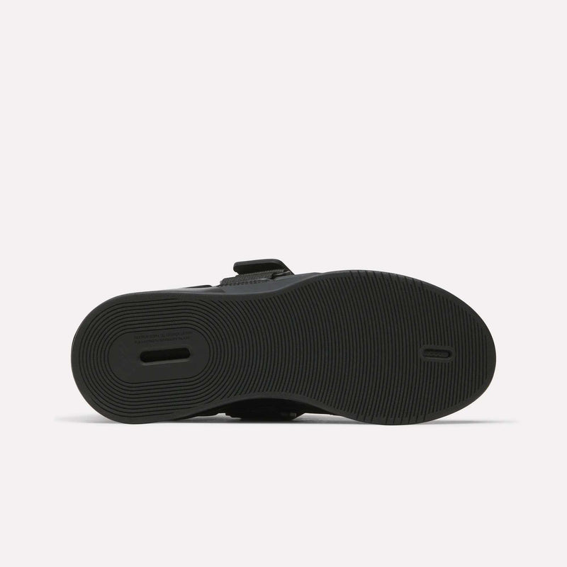 The image displays the black rubber sole of Reebok Women's Legacy Lifter IV Training Shoes, with a textured circular tread and a rectangular heel cut-out for support. The shoe is shown sole-up on a plain white background.