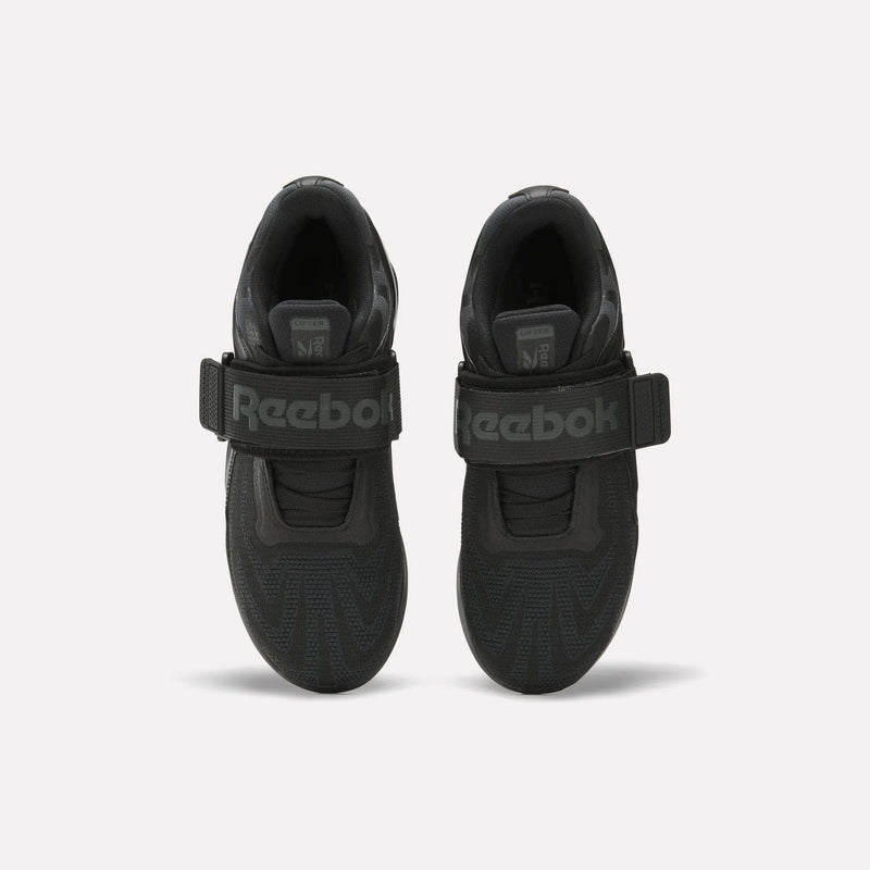 A pair of Reebok Women's Legacy Lifter IV Training Shoes in black, shown from above, featuring thick support straps across the top, gray Reebok logo, and textured toe patterns.