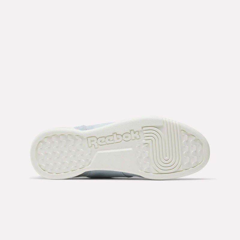 The image shows the white rubber sole of the Reebok Women's Workout Plus Shoes, viewed from below. The sole features the Reebok logo and a mix of hexagonal and linear patterns, reflecting classic '80s fitness style.