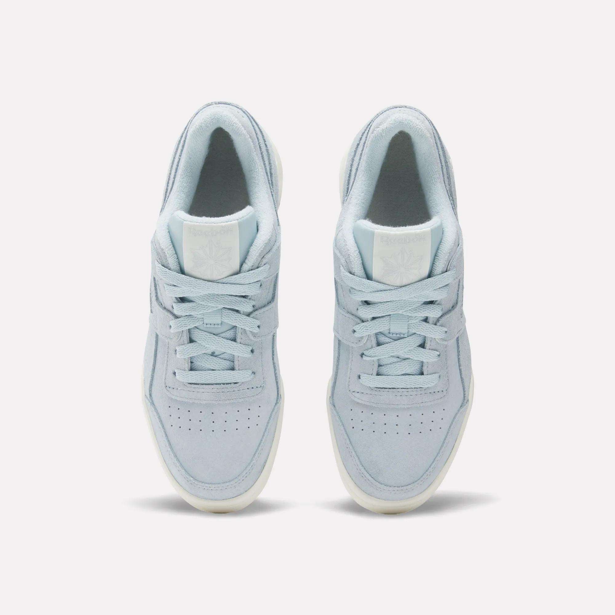 A top view of the Reebok Women's Workout Plus Shoes in light blue with white soles, laces, toe perforations, and a subtle logo on the tongue, inspired by '80s fitness style, set against a plain white background.