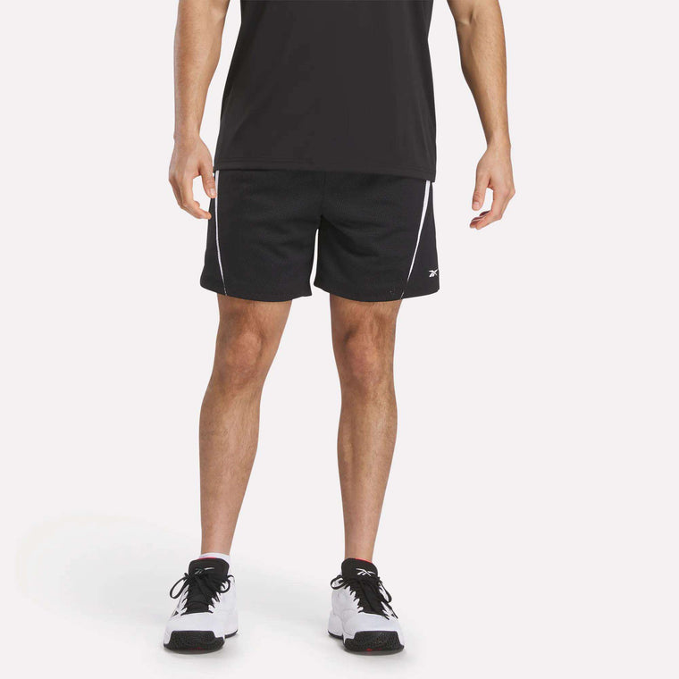 A man stands against a plain white background wearing a black t-shirt, Reebok Mesh Shorts in black with white trim featuring breathable mesh for comfort, and white and black sneakers. His face is not visible.