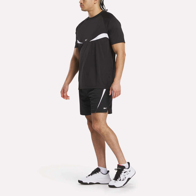 A person stands sideways against a plain white background, dressed in a black and white athletic outfit featuring Reebok Mesh Shorts and a breathable mesh T-shirt with white sneakers.