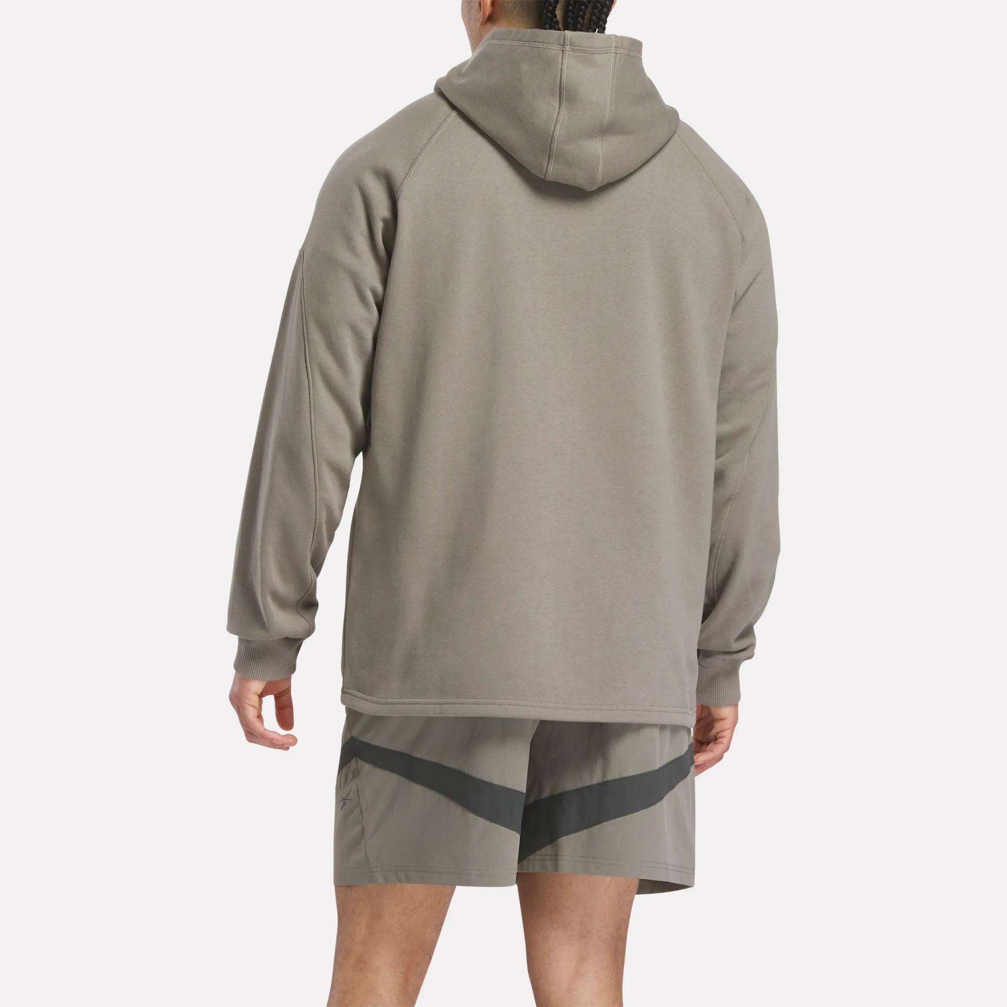 A person faces away from the camera, wearing a taupe Reebok French Terry Basketball Hoodie and matching shorts with a dark diagonal stripe, set against a plain light background.