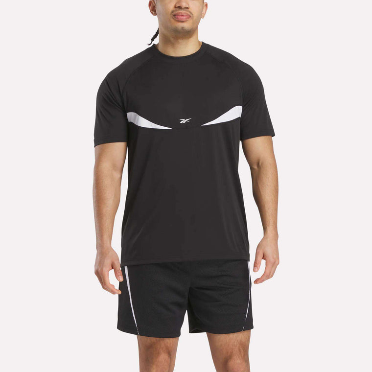 A man stands facing forward against a plain white background, wearing a black Reebok Warm-Up Basketball T-Shirt with white accents and matching black training shorts.