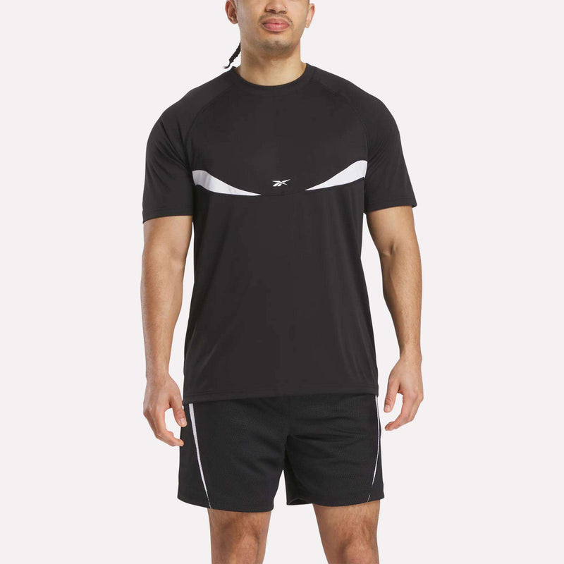 A man stands facing forward against a plain white background, wearing a black Reebok Warm-Up Basketball T-Shirt with white accents and matching black training shorts.