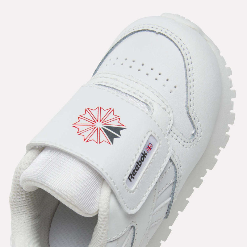 Close-up of Kids' Classic Leather Shoes by Reebok, featuring a white design, Velcro strap with the Reebok logo, red and black starburst, small Union Jack, and perforated toe for breathability—perfect stylish shoes for everyday wear.