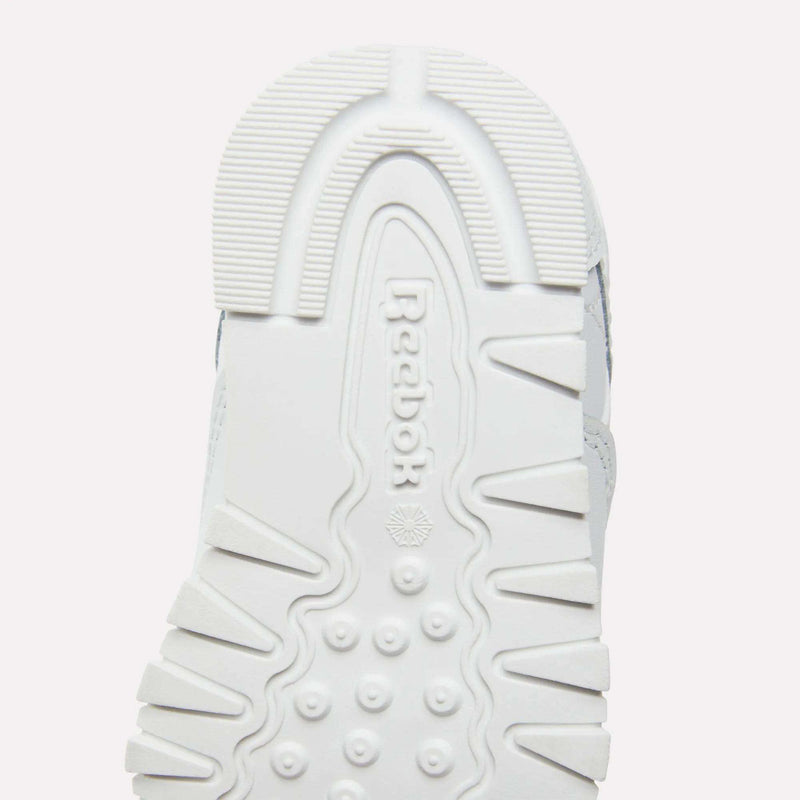 Close-up of the white rubber outsole on Reebok Kids' Classic Leather Shoes, showing the Reebok logo and a textured tread with ridges, dots, and geometric patterns for grip—ideal for everyday wear.