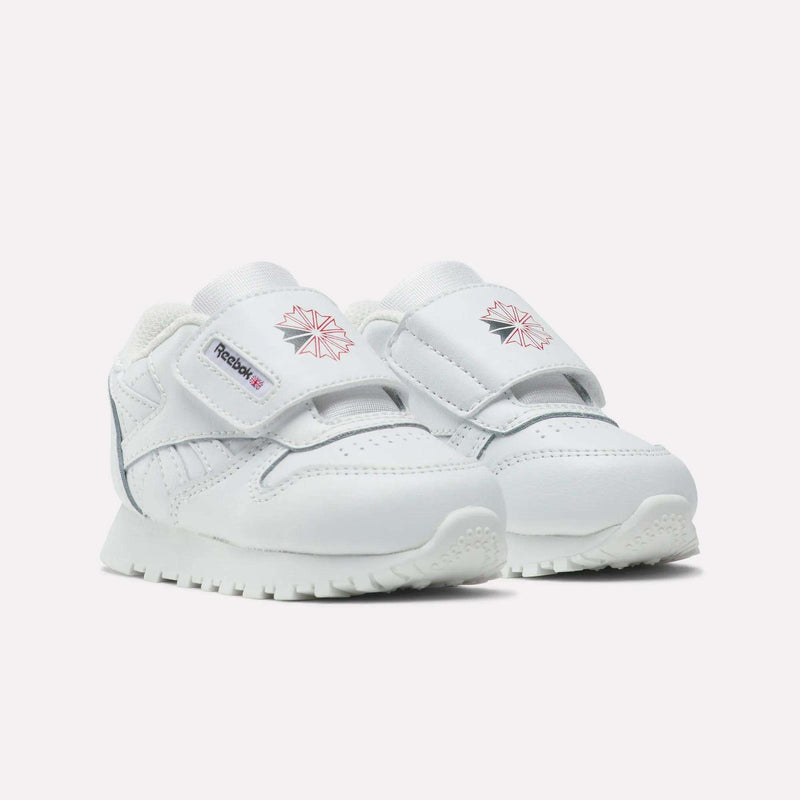 The Reebok Kids' Classic Leather Shoes are white toddler sneakers with Velcro straps, pink Reebok logos on the sides and tongues, and textured white soles—ideal for casual everyday wear, shown on a plain white background.