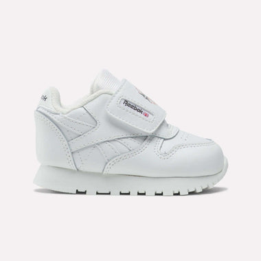 The Reebok Kids' Classic Leather Shoes feature a white low-profile design, hook-and-loop strap, and rubber sole. Logo accents on the strap and side provide a timeless look—ideal for everyday toddler wear.
