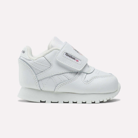The Reebok Kids' Classic Leather Shoes feature a white low-profile design, hook-and-loop strap, and rubber sole. Logo accents on the strap and side provide a timeless look—ideal for everyday toddler wear.