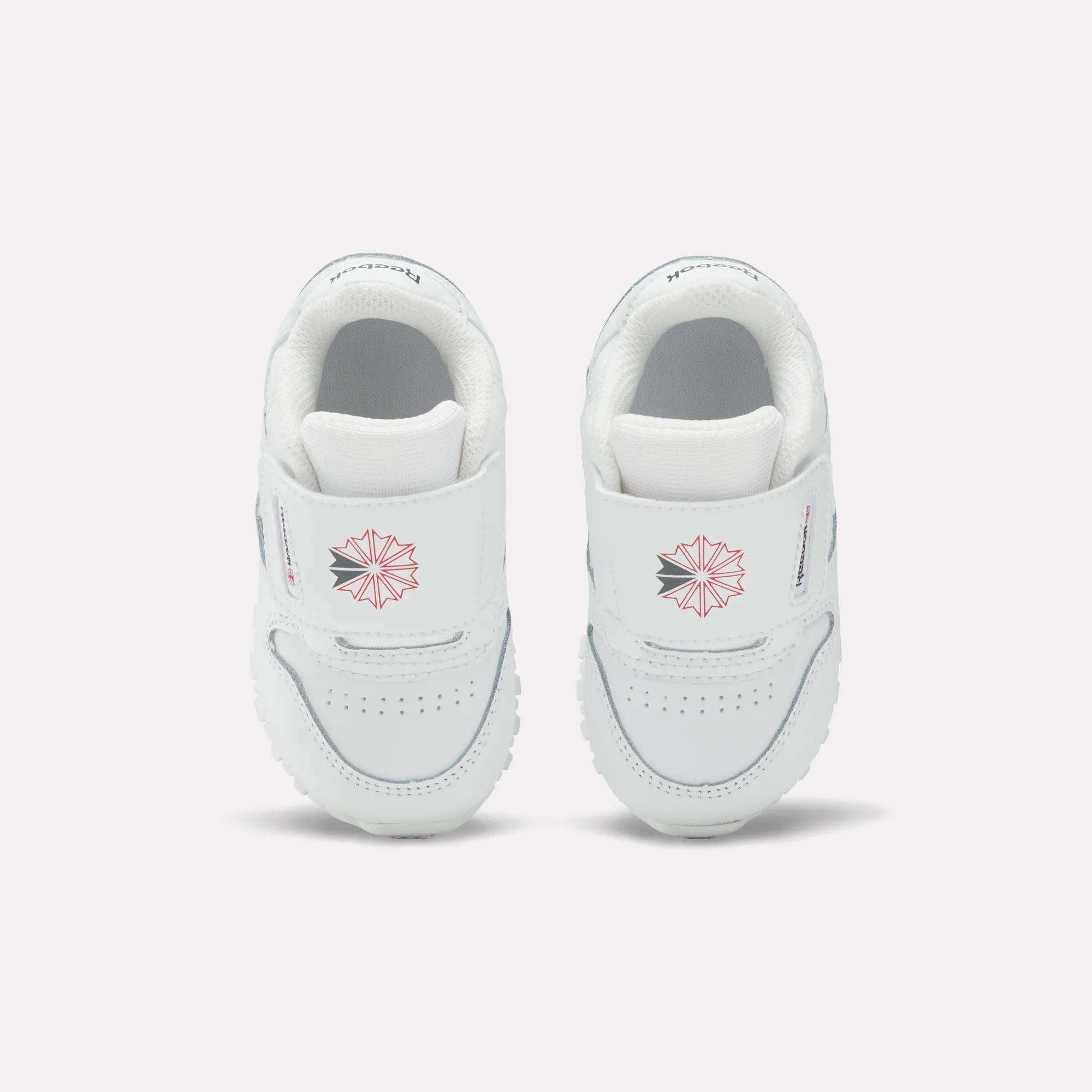 Kids' Classic Leather Shoes by Reebok for babies feature white leather, Velcro straps, a pink geometric star design, and small front text—ideal for everyday wear and shown on a plain light background.