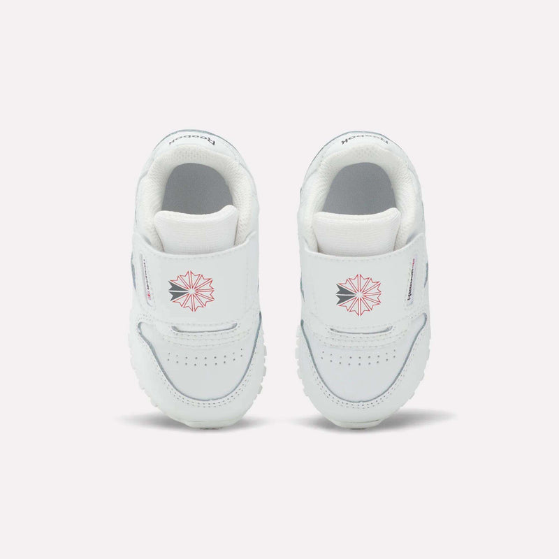 Kids' Classic Leather Shoes by Reebok for babies feature white leather, Velcro straps, a pink geometric star design, and small front text—ideal for everyday wear and shown on a plain light background.