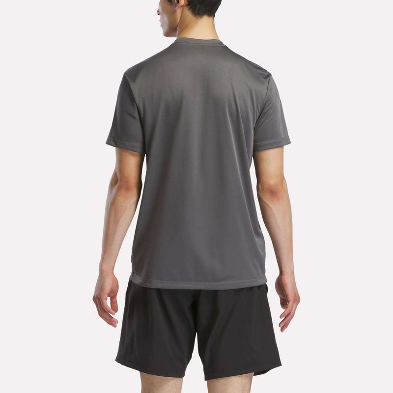 A person stands with their back to the camera, wearing a Reebok Men's Short Sleeve Tech Training T-Shirt in gray and black athletic shorts, highlighting its sweat-wicking comfort for active workouts against a plain light background.