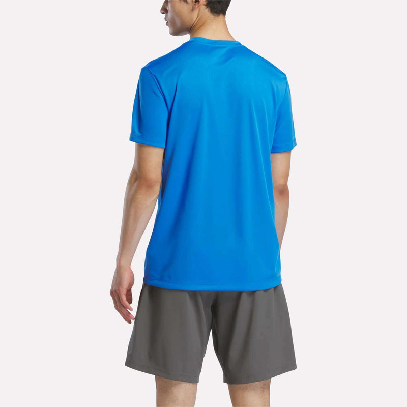 A person in a Men's Short Sleeve Tech Training T-Shirt by Reebok in bright blue and gray shorts stands with their back to the camera against a plain white background.