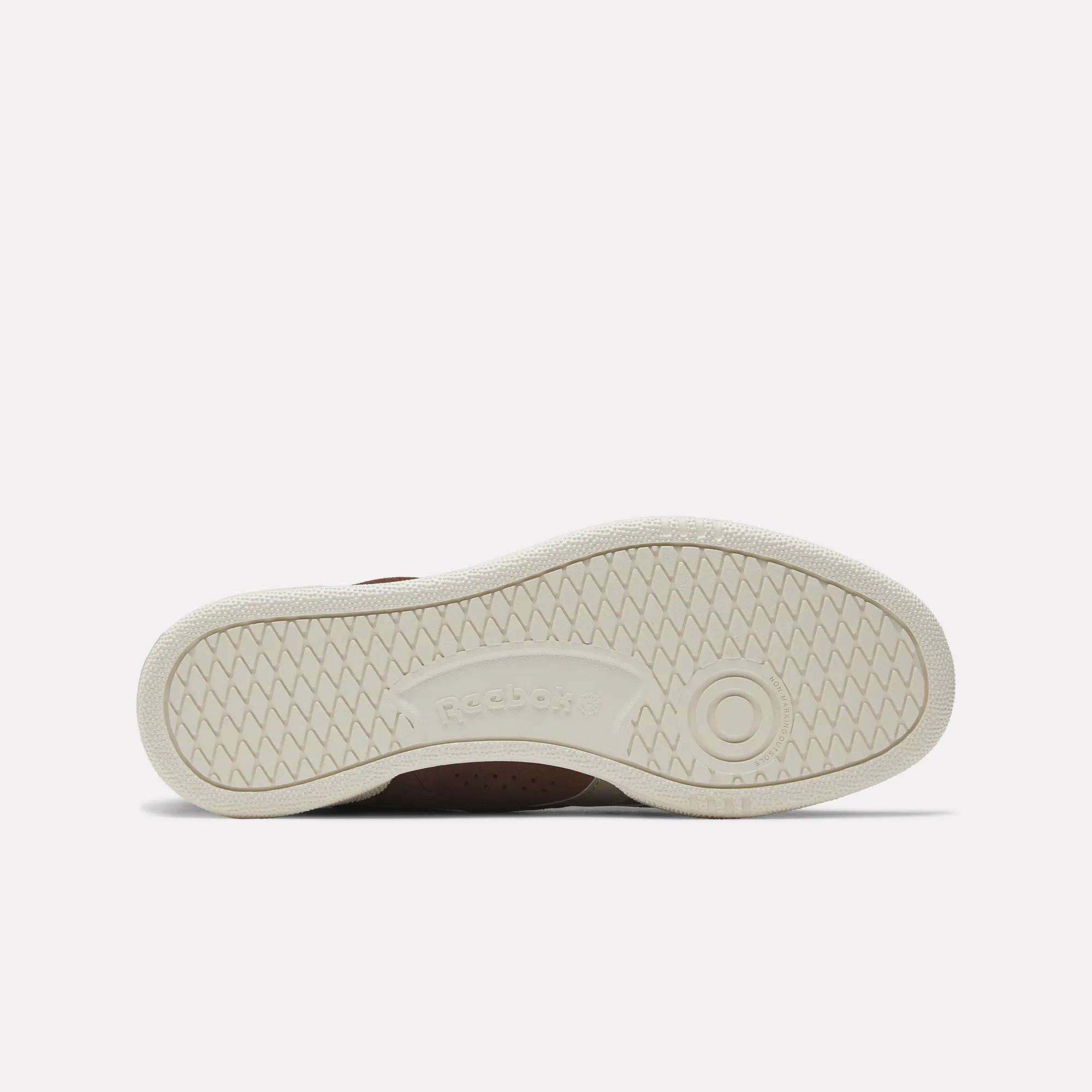 The image displays the sole of the Reebok Club C Grounds UK Shoes, with an off-white rubber base, herringbone tread pattern, circular grip accents, and the embossed Reebok logo in the center.