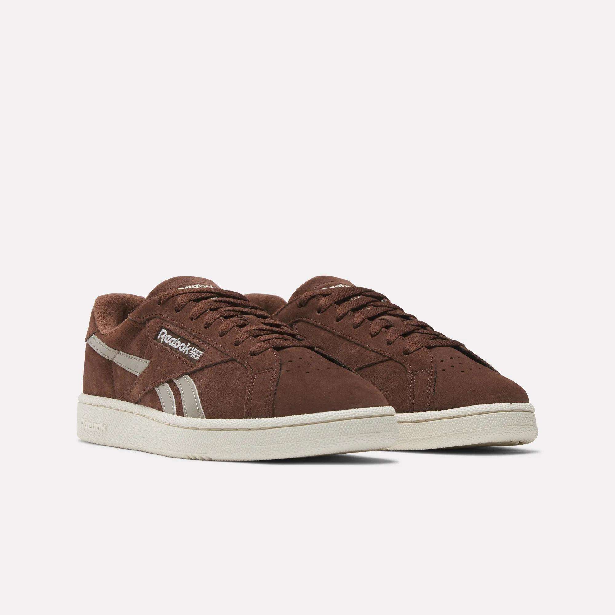 The Reebok Club C Grounds UK Shoes feature brown suede uppers, white accents, and off-white rubber soles, capturing the vintage charm of classic tennis sneakers. They are shown side by side against a plain white background.