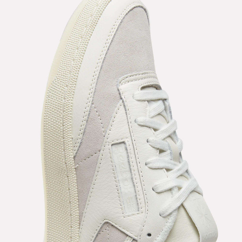 A close-up of the Reebok x IDEA Club C 85 Shoes in white and light gray, featuring white laces, signature side details, a textured sole, and Reebok branding—styled against a light background and ideal for pairing with your favorite vintage reads from the IDEA bookstore.