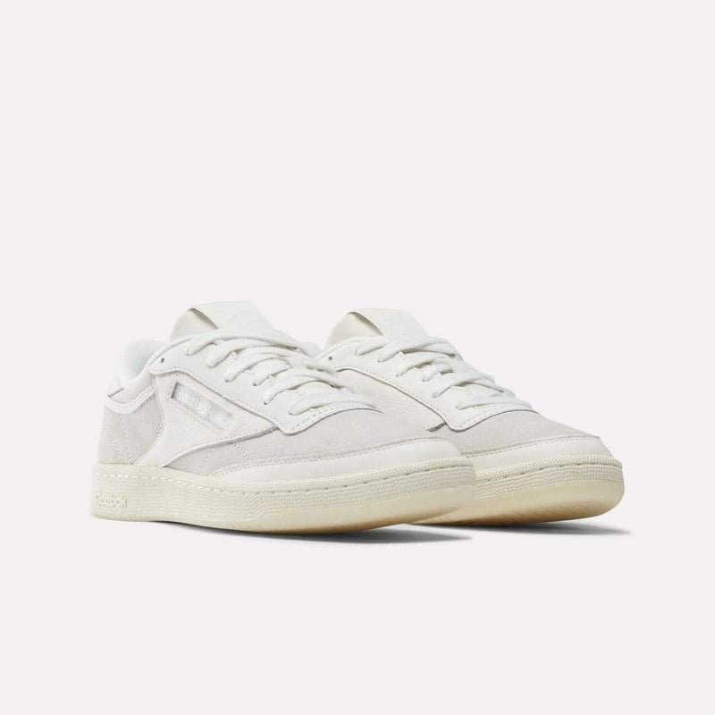 The Reebok x IDEA Club C 85 Shoes—an off-white, low-top style by Reebok featuring suede and leather accents, white laces, and cream-colored soles—are photographed on a plain white background, evoking the timeless look you’d discover while leafing through vintage books at the IDEA bookstore.