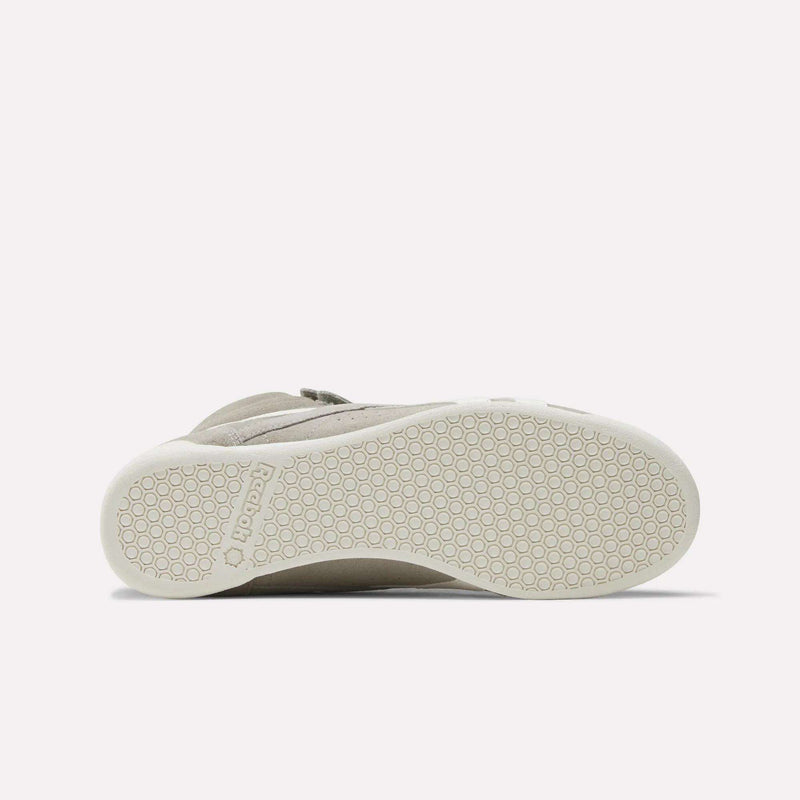 The image shows the bottom view of a beige Women's F/S Hi Shoe by Reebok, with a white sole featuring a hexagonal pattern and the Reebok name embossed near the heel, reflecting popular high top sneaker design trends.