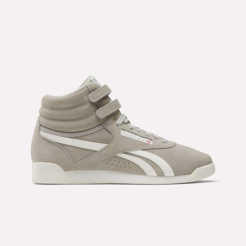 The Reebok Women's F/S Hi Shoes are light grey high top sneakers with a suede upper, white accents, double ankle straps, a stripe detail, small flag logo, and white sole—shown from the side.