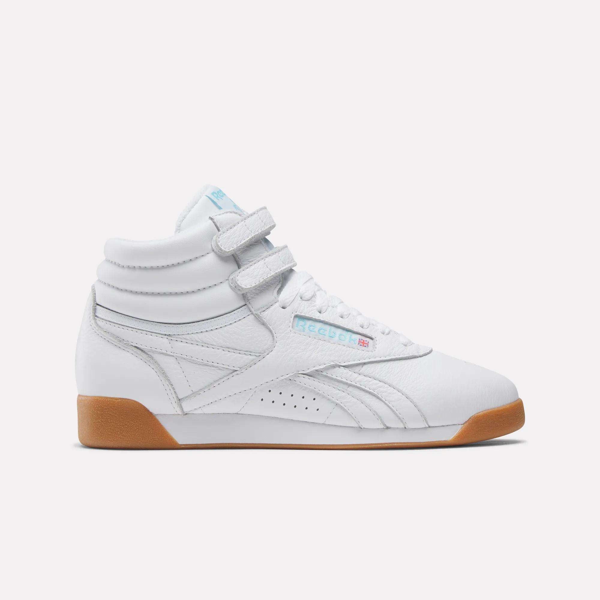 The Reebok Women's Freestyle Hi Shoes are white high-top sneakers with two velcro straps, light blue accents, a gum sole, and the Reebok logo on the side—an 80s-inspired classic shown from the side on a plain white background.