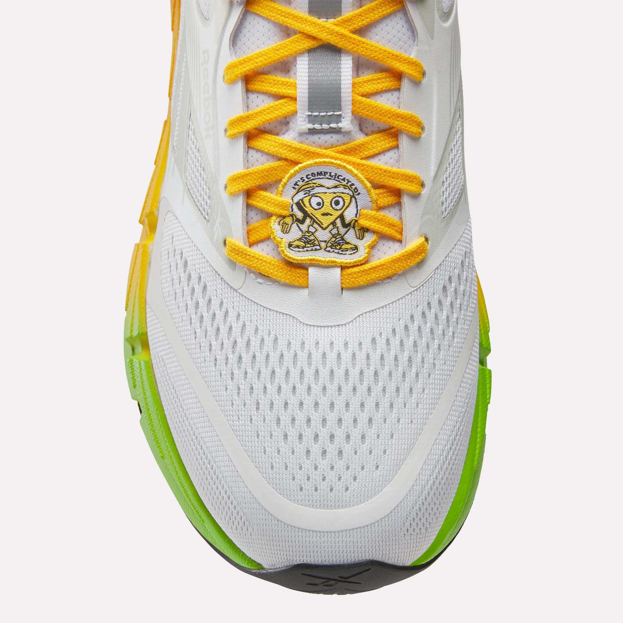 Reebok Men's FloatZig 2 SoleMates Running Shoes feature white uppers, yellow laces, a cartoon heart patch with "Act Confidently," lightweight foam midsoles, and green-yellow sole accents for comfort and style.