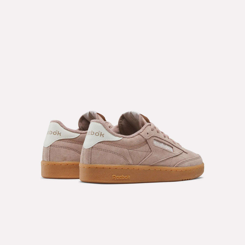 A pair of Women’s Club C 85 Shoes by Reebok in mauve, featuring soft suede uppers, white heel accents, and gum rubber soles, are displayed against a plain white background. The sneakers are angled to showcase both the side and back views.