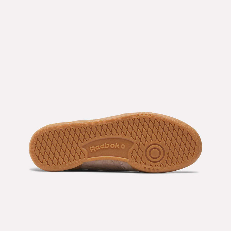 The image displays the sole of the Reebok Women’s Club C 85 Shoes, crafted from brown rubber with a textured herringbone tread pattern and featuring the Reebok logo embossed at the center.