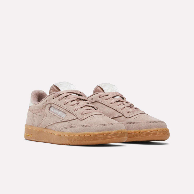 A pair of Women’s Club C 85 Shoes by Reebok in light pink, showcasing a soft suede upper, gum rubber soles, white tongue labels, and classic Reebok branding on the side, displayed against a plain white background.