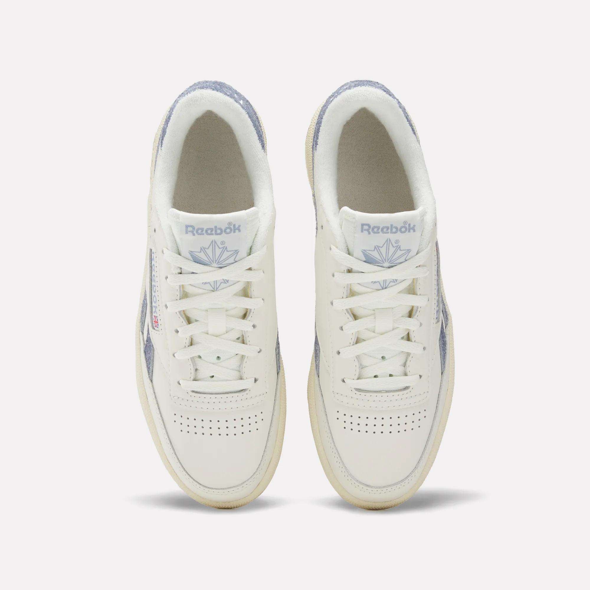 A top view of Reebok Women's Club C Revenge Shoes shows white sneakers with light purple accents, perforated toe boxes, and the Reebok logo with a purple emblem on the tongues.
