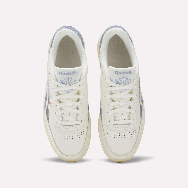 A top view of Reebok Women's Club C Revenge Shoes shows white sneakers with light purple accents, perforated toe boxes, and the Reebok logo with a purple emblem on the tongues.