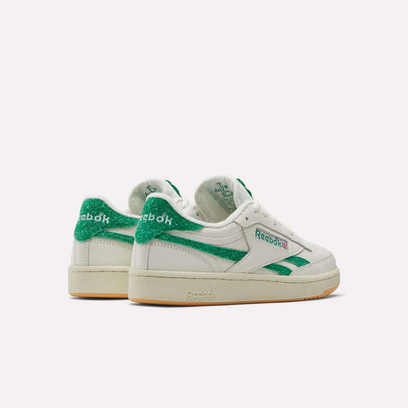 A pair of Reebok Women’s Club C Revenge Shoes in white with green accents and beige soles, displayed from the back and side on a plain white background.