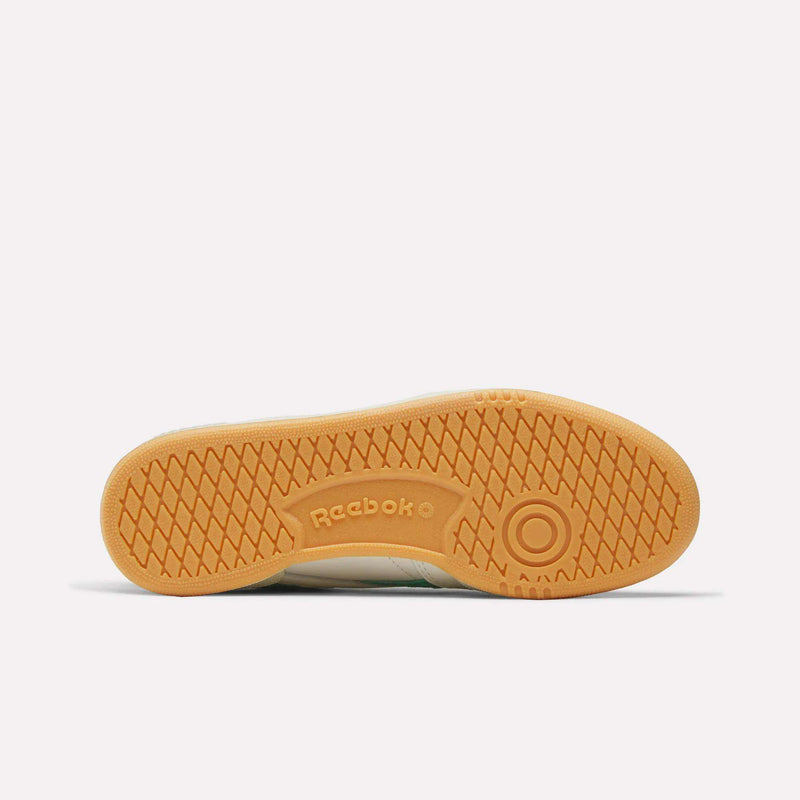 The image displays the bottom view of the Reebok Women’s Club C Revenge Shoes, featuring a light brown rubber sole with the signature Reebok logo and a circular traction pattern near the heel—an iconic detail found in many women’s court sneakers.