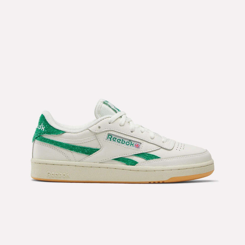 A Reebok Women’s Club C Revenge Shoe in Chalk/Linen/Teamgreen is displayed from a side angle against a plain white background, featuring green Reebok branding and accents with a beige rubber sole. This classic women’s court shoe blends timeless style with everyday comfort.