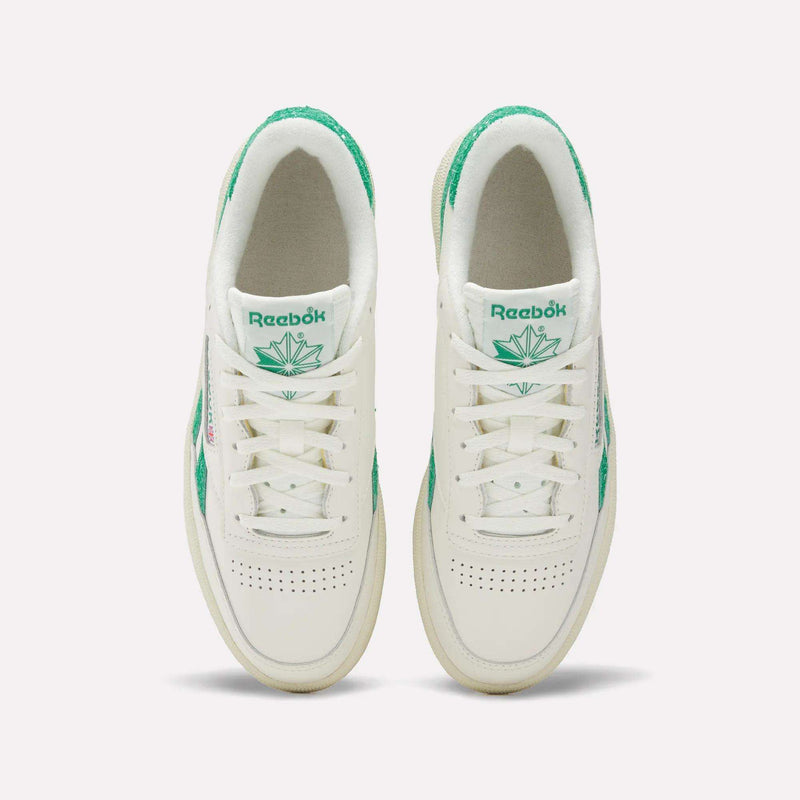 Top view of a pair of Reebok Women’s Club C Revenge Shoes in white with green accents and a green leaf logo on the tongue, placed side by side on a plain white background.