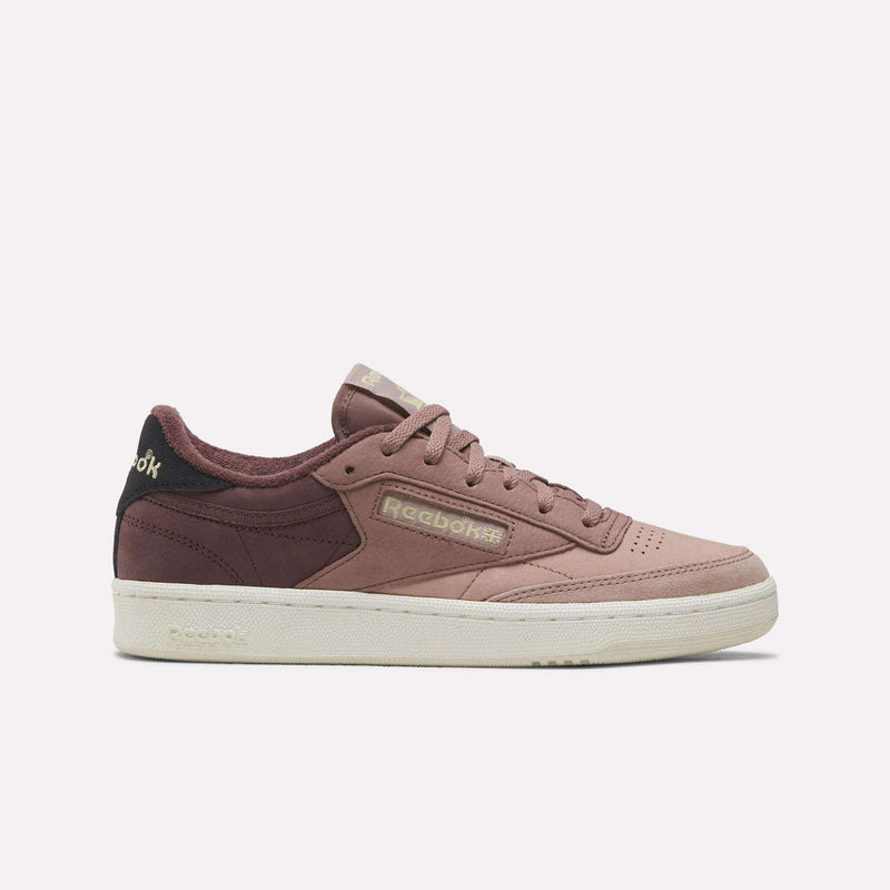 The Women’s Club C 85 Shoes by Reebok, displayed in a sleek side profile against a simple light backdrop, feature a Rosewood and Light Cocoa nubuck leather upper with a Chalk white sole—an effortlessly stylish choice for any women’s tennis shoe collection.