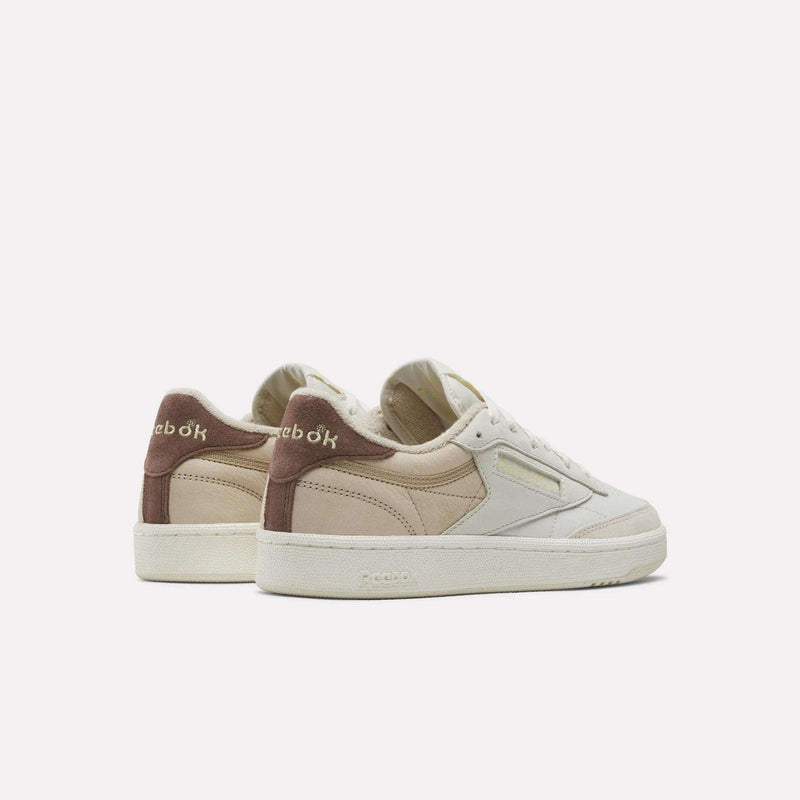 A pair of Reebok Women’s Club C 85 Shoes, featuring beige, cream, and brown suede accents in premium nubuck leather, is shown from the back and side against a plain white background. These classic Reebok sneakers combine timeless style with modern comfort.