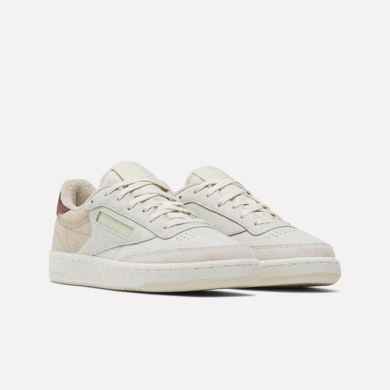 A pair of Reebok Women’s Club C 85 Shoes in off-white nubuck leather with beige accents and textured soles, styled as low-top tennis sneakers, displayed against a plain white background.