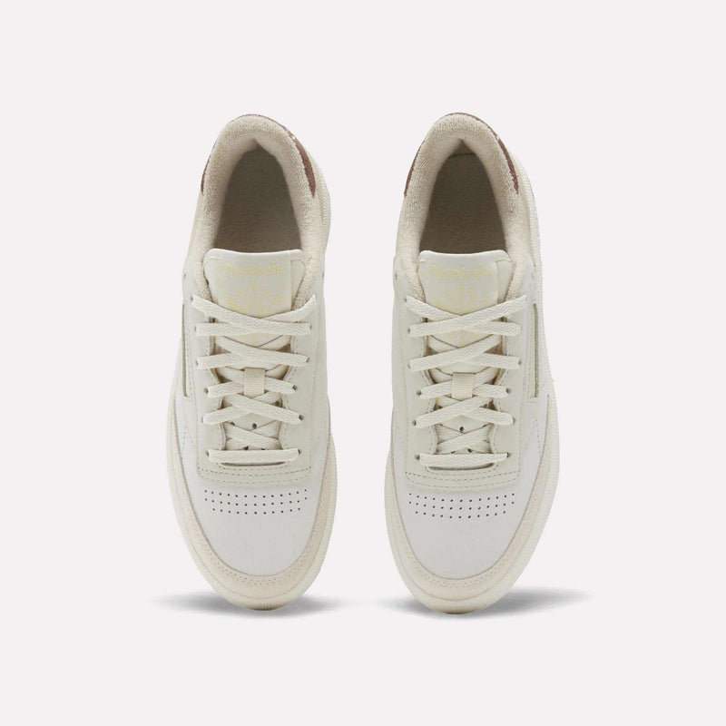 A pair of off-white Reebok Women’s Club C 85 Shoes is shown from above, highlighting the laces, perforated toe boxes, and cream-colored lining against a plain light background. These classic sneakers feature premium nubuck leather for a soft, refined finish.