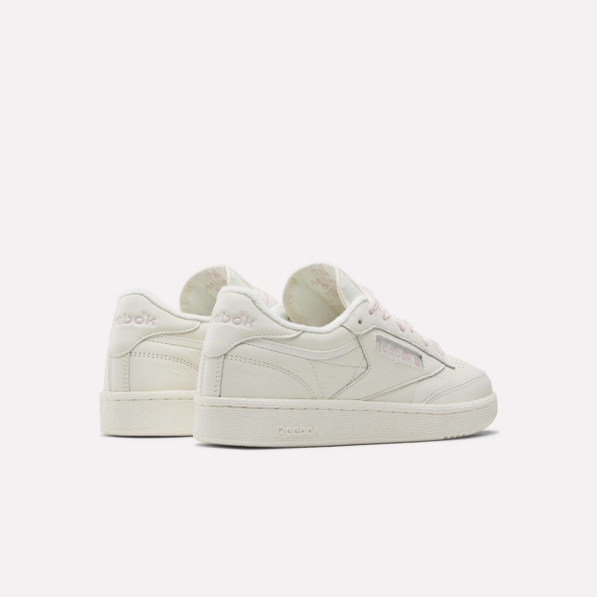 The Women's Club C 85 Vintage Shoes by Reebok are shown in off-white leather with pale pink accents and laces, featuring both side and back views on a plain white background for a chic vintage style.