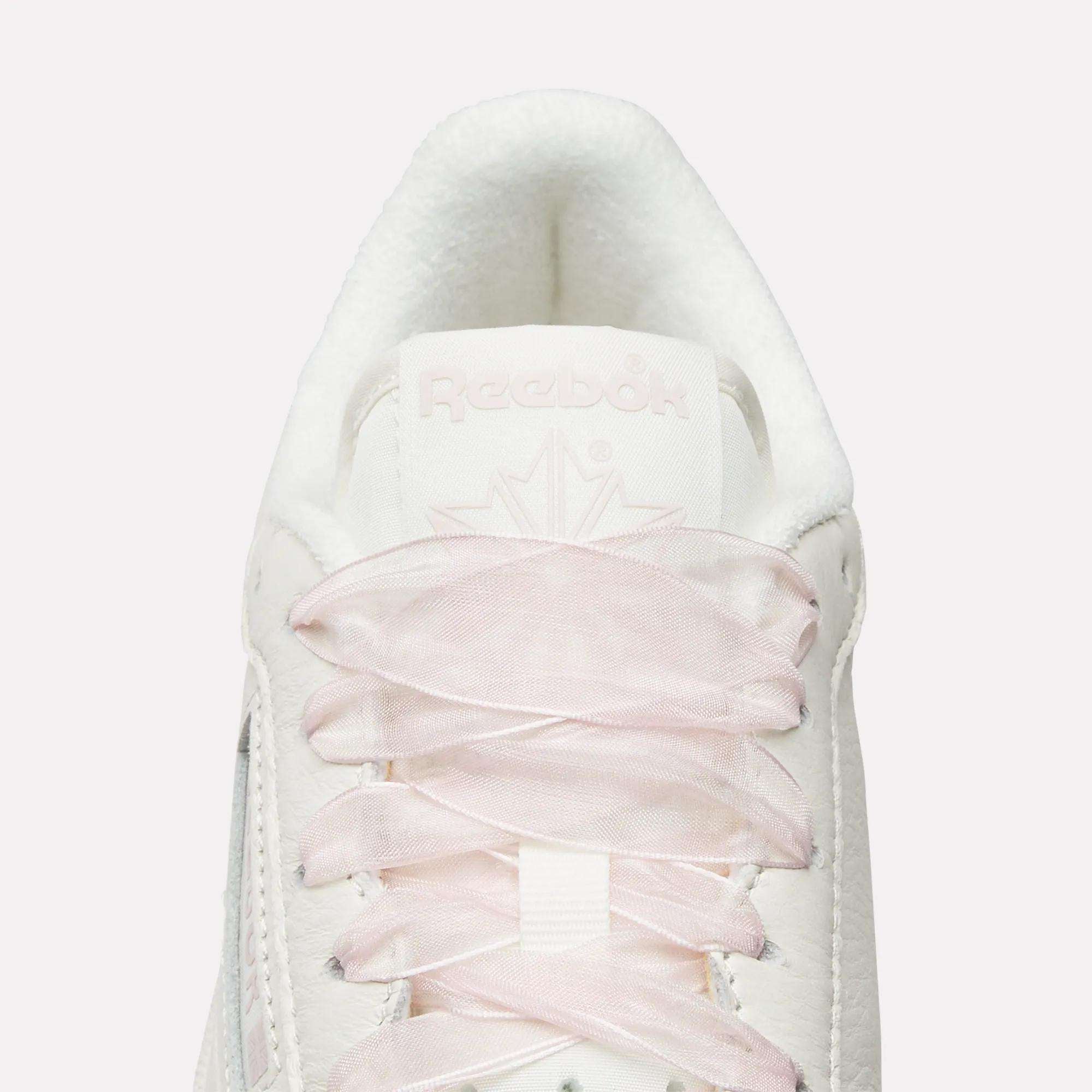 Top view close-up of Reebok Women's Club C 85 Vintage Shoes in white, featuring light pink laces, a white tongue, embossed Reebok branding, and a subtle maple leaf design for a vintage-inspired look.