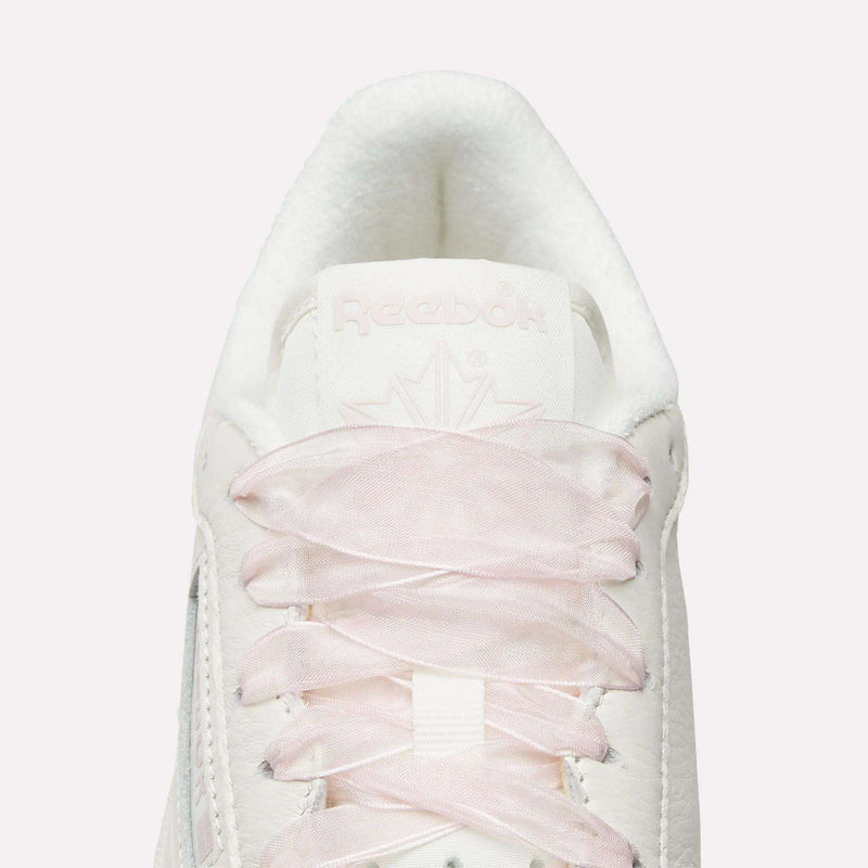 Top view close-up of Reebok Women's Club C 85 Vintage Shoes in white, featuring light pink laces, a white tongue, embossed Reebok branding, and a subtle maple leaf design for a vintage-inspired look.