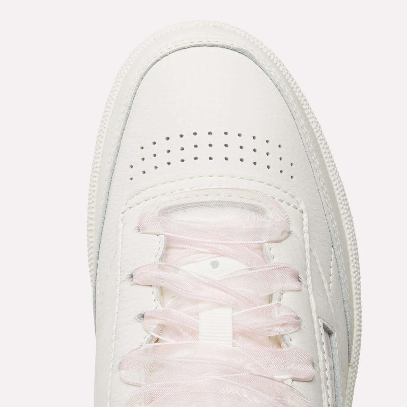 Top view of Women's Club C 85 Vintage Shoes by Reebok in white with light pink laces and toe perforations for ventilation, photographed on a plain white background.