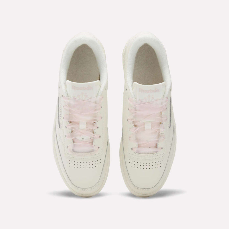 Top view of Women's Club C 85 Vintage Shoes by Reebok—white leather shoes with light pink translucent laces, perforated toe boxes, and subtle branding on the tongues, arranged side by side for a clean vintage look.