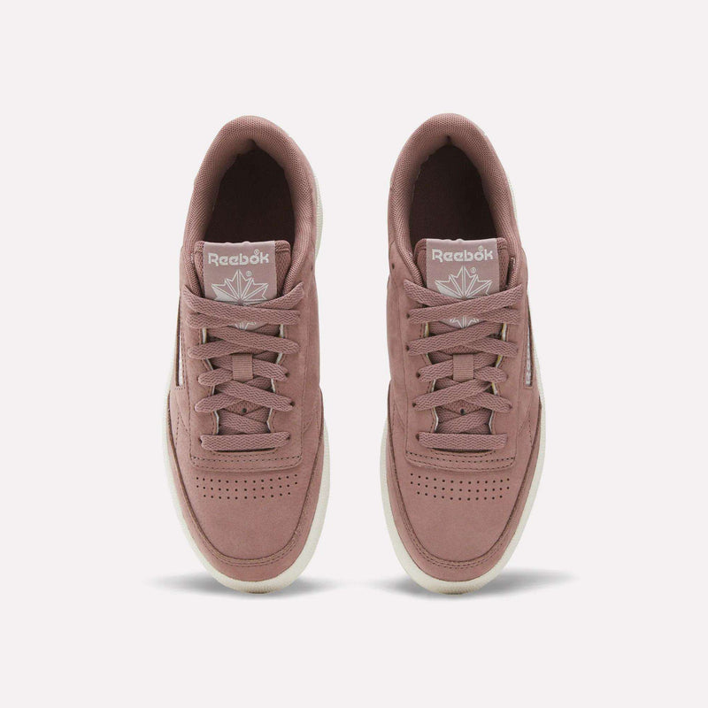 A pair of Reebok Women’s Club C 85 Shoes in mauve with white soles is shown from above, highlighting the laces and Reebok logo on each tongue against a plain white background—these classic sneakers deliver a modern update to women’s tennis footwear.