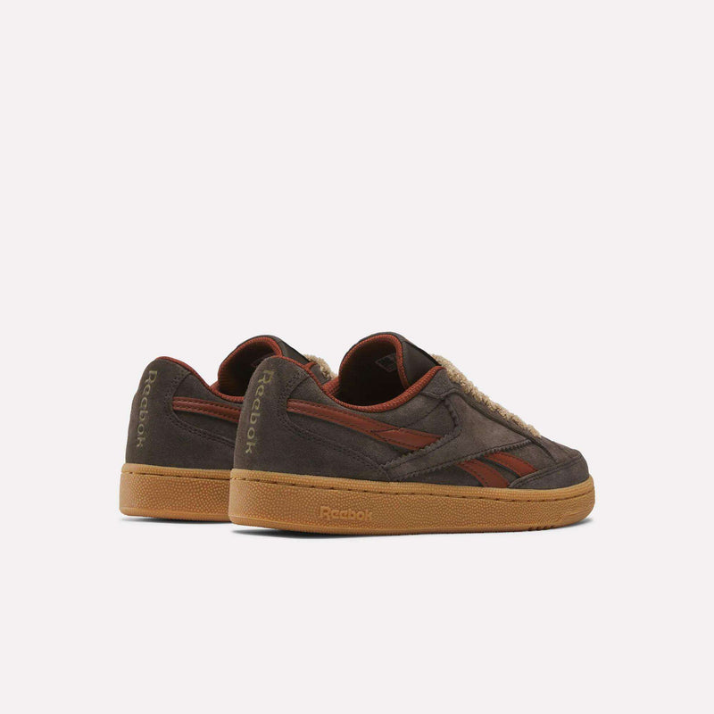 A pair of Reebok Women’s Club C Grounds 70 Shoes in brown suede, featuring gum soles, red accents, and textured detailing on the sides and heel, are displayed on a white background with the sneakers angled slightly apart. These retro-inspired shoes combine classic style with contemporary comfort for women.