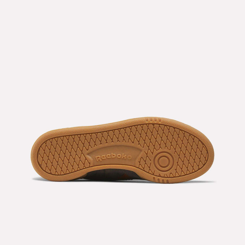 The outsole of the Women’s Club C Grounds 70 Shoes by Reebok is shown from the bottom in a brown gum color, featuring a textured grip pattern and an embossed Reebok logo at the center—classic touches inspired by vintage sneakers and enduring style.